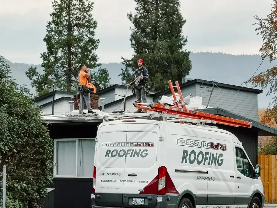 A branded Pressure Point Roofing van parked at a Southern Oregon home while the crew works on the roof