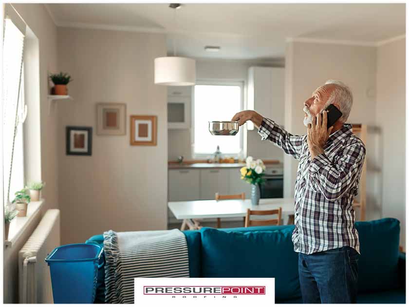 Man on phone holding a metal bowl to catch ceiling drip
